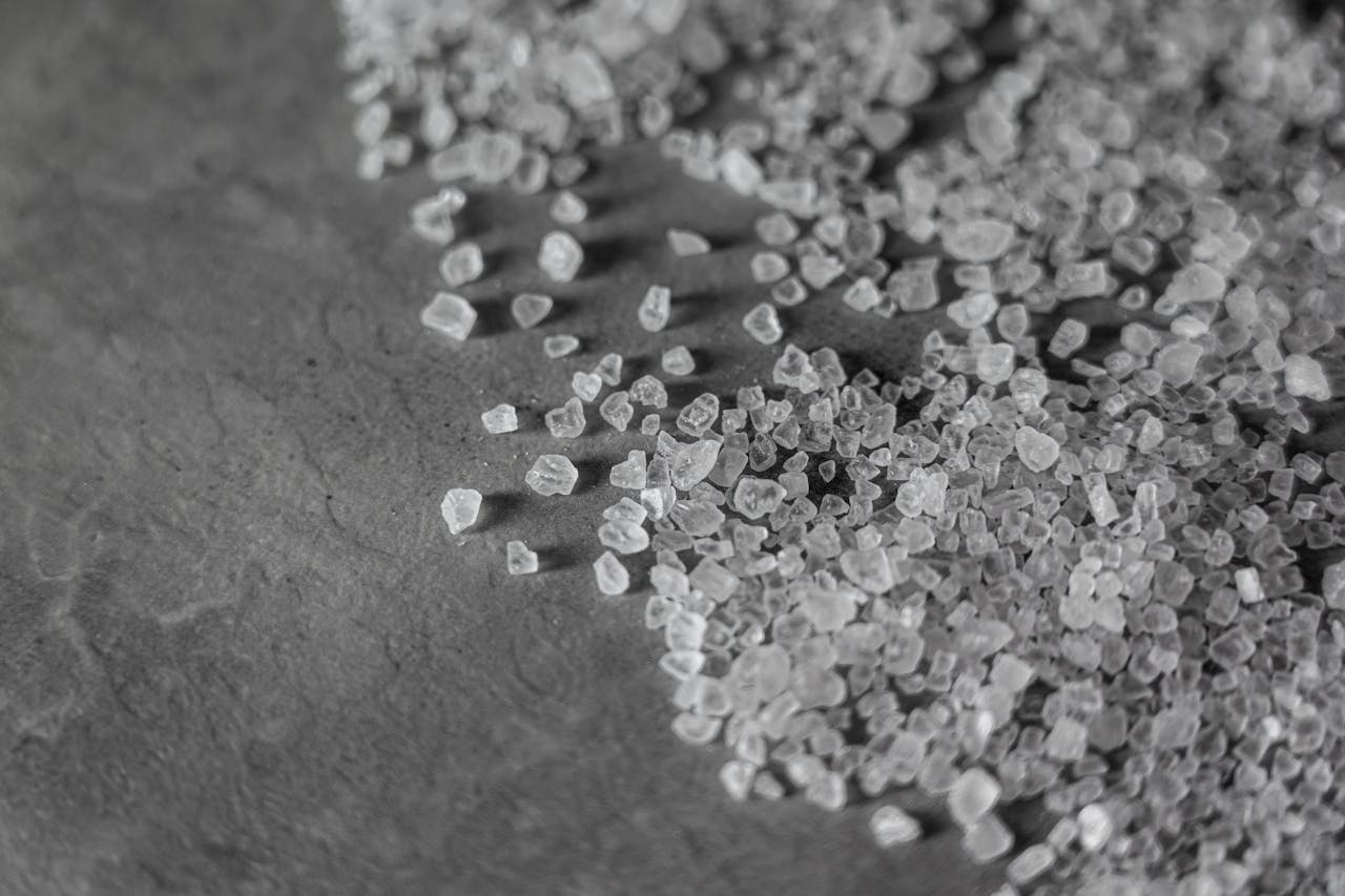 Close-up monochrome image showcasing the texture and shape of rock salt granules on a surface.